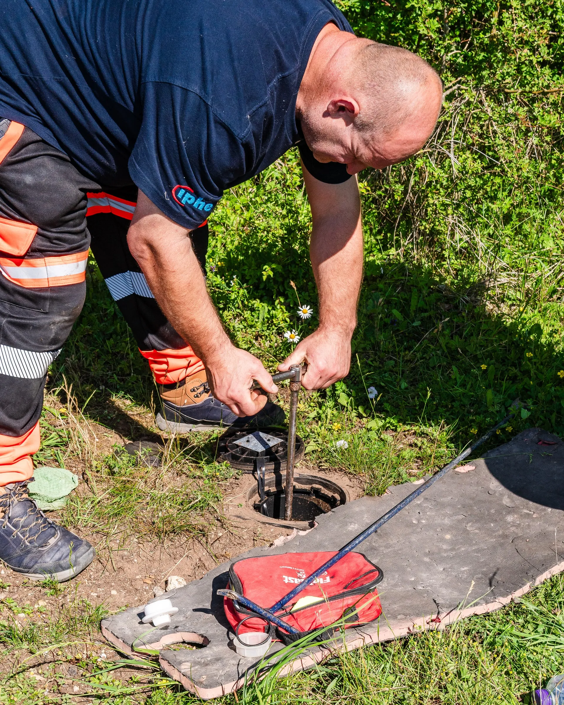 Engineer kneeling at an open meter chamber in a grass verge, checking the meter